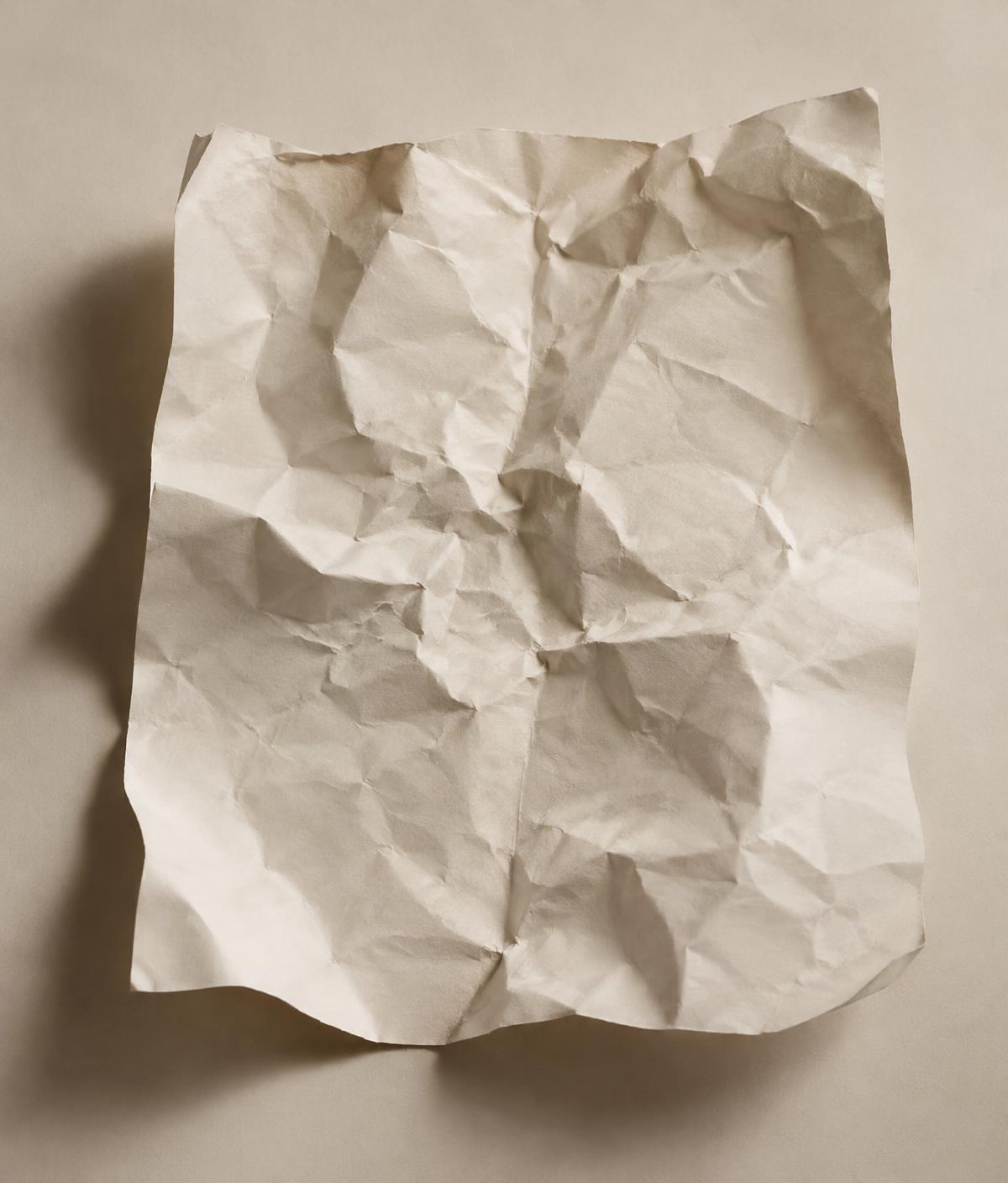 A sheet of off-white paper, crumpled and then opened flat, its folds catching soft light